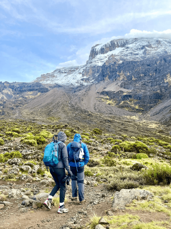 trekking essenciais → Strike Tours Na imagem, é possível observar duas pessoas com os equipamentos essenciais para o percurso do trekking ao cume do Kilimanjaro, na Tanzânia.