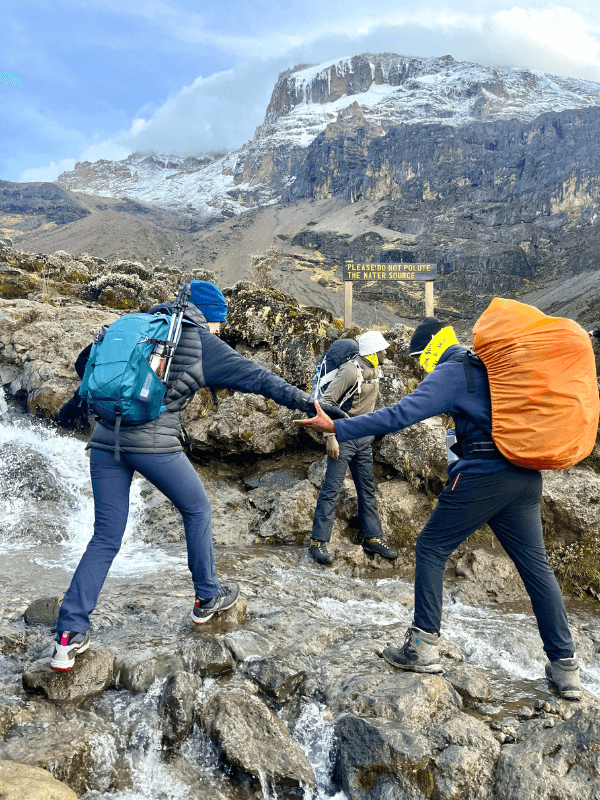 trekking personalidade → Strike Tours Na imagem, é possível observar uma das características mais importantes das pessoas que praticam trekking: o espírito de equipa. Esta descreve uma pessoa a dar a mão a outra pessoa para atravessar um riacho.